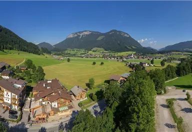 A picturesque landscape with green meadows, mountains in the background, and a small village. The sky is clear and sunny.