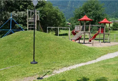 A playground with two pieces of equipment and a slide. In the background, there is a green meadow and trees.