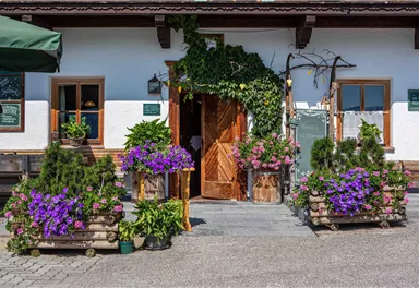 An inviting entrance area with colorful flowers and plants. The wooden terrace and the white walls give the place a charming, rustic character.