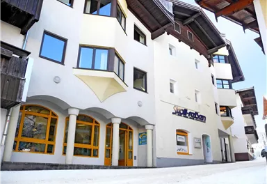 A modern building with a bright facade and large windows. The lower floors have storefronts with bright frames, and the street is paved.