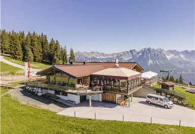 An alpine mountain hut with a beautiful view of the mountains. Surrounded by trees and green grass, it offers an inviting atmosphere.