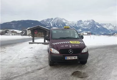 A taxi is standing on a snow-covered road with a picturesque mountain landscape in the background. The surroundings are wintry and tranquil.