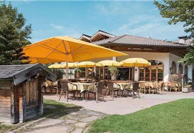 An inviting restaurant with yellow sun umbrellas and a cozy terrace. The surrounding green space and the trees create a pleasant atmosphere.