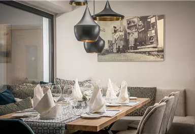 Ein gemütliches Restaurant mit einem schön gedeckten Tisch und eleganten Stühlen. Über dem Tisch hängen stilvolle Lampen und es gibt ein Vintage-Bild an der Wand.