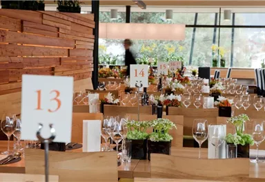 Ein elegantes Restaurant mit schön dekorierten Tischen und Blumenarrangements. Die Tische sind mit Gläsern und nummerierten Schildern versehen.