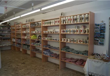 Ein Geschäft mit mehreren Regalen, die verschiedene Souvenirs und Gläser zeigen. Der Raum hat einen hellen, einladenden Eindruck.