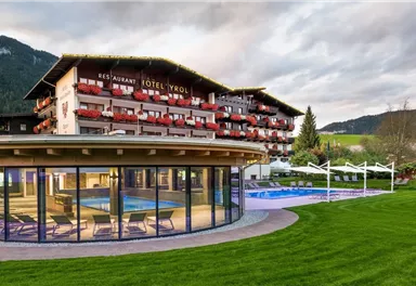 Ein modernes Hotel mit einem großen Garten und einem Außenpool. Im Hintergrund sind Berge und eine schöne Landschaft zu sehen.