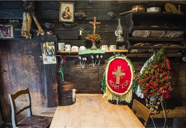 Ein rustikaler Raum mit einem Holzstuhl und einem Tisch. Die Wände sind mit traditionellen Gegenständen und Dekorationen geschmückt.