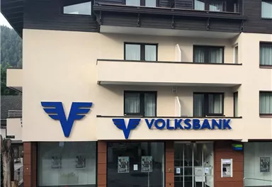A modern building with the Volksbank logo on the facade. The area is quiet and surrounded by natural elements.