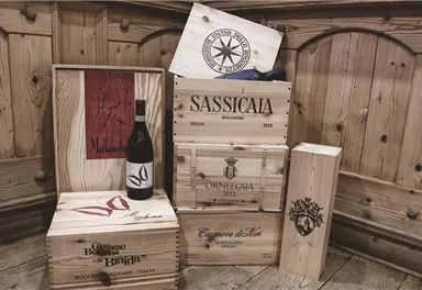 A collection of wooden boxes with wines and a bottle of Sassicaia. The background consists of rustic wood.