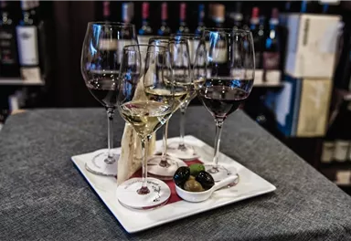A stylish presentation of wine in four glasses on a tray. Also included are a small portion of olives and a snack.