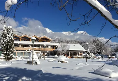 A picturesque hotel in the snow with a serene winter landscape. The mountains are visible in the background and the sky is clear and blue.