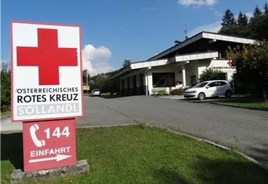 A building of the Austrian Red Cross in Söllandl. In the foreground is a large red cross sign with the phone number 144.