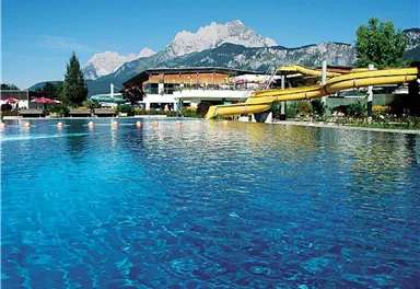 A sparkling pool with a yellow water slide and a beautiful mountain landscape in the background. A relaxing place, perfect for a day by the water.
