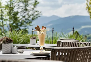 A delicious milkshake with cream and cookies is on a table outside. In the background, green hills and trees are visible.
