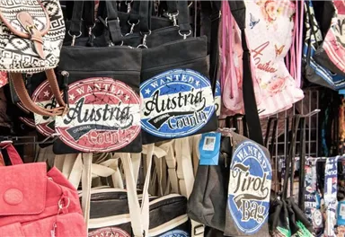 Eine Auswahl an verschiedenen Taschen hängt an einem Verkaufsstand. Einige Taschen sind mit dem Aufdruck „Austria“ und „Tirol“ versehen.