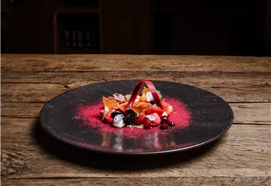 An artistically arranged dessert plate on a black plate. Fresh fruits and an elaborate decoration create an appealing visual effect.