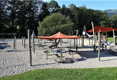 A playground with a sand floor and various play equipment. Shade segments provide protection from the sun.