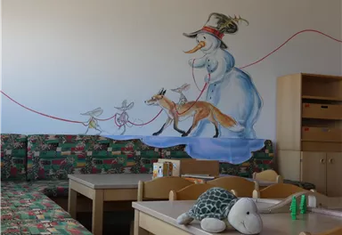 Eine fröhliche Wandmalerei zeigt einen Schneemann, der einen Fuchs und eine Maus an einer Leine führt. Der Raum ist hell und einladend mit bunten Möbeln und Spielzeug.