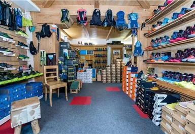 A store with a variety of shoes and backpacks.
Shelves are filled with sports items, and the floor is carpeted.