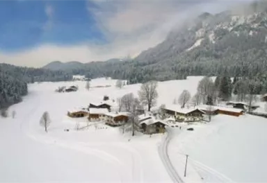 A picturesque winter landscape with snow-covered hills and traditional wooden houses. The sky is clear and blue, and the surroundings radiate tranquility.