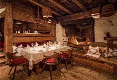 A cozy restaurant with a wood stove and rustic decor. The table is set for guests and the atmosphere is warm and inviting.