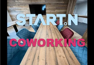 A modern coworking area with a long wooden table. The environment is designed with colorful chairs and warm wood paneling.