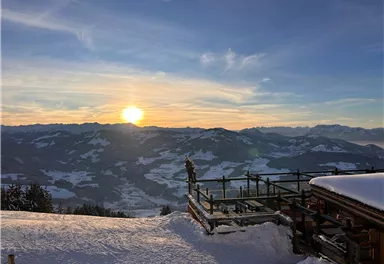 Eine malerische Berglandschaft im Schnee mit einem Sonnenuntergang am Horizont. Die Aussicht zeigt schneebedeckte Berge und eine ruhige Atmosphäre.