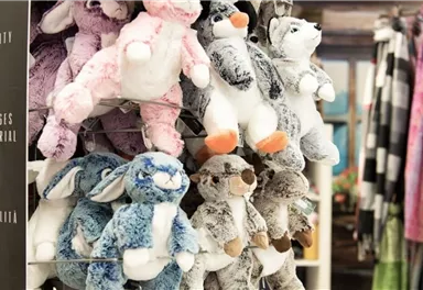 Eine Auswahl an kuscheligen Plüschtieren in verschiedenen Farben hängt an einem Regal. Die Tiere sind bunt und freundlich gestaltet.