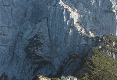 Eine beeindruckende Berglandschaft mit steilen Felsen und einer schönen Wiese im Vordergrund. Im Hintergrund erhebt sich majestätisch der Felsen.