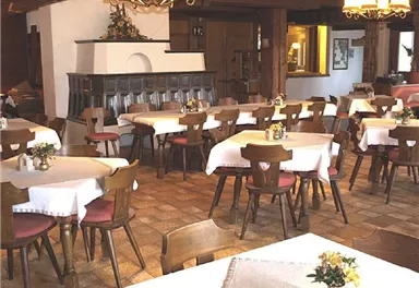 A cozy restaurant with wooden chairs and tables covered with white tablecloths. The atmosphere is inviting and rustic, with warm lighting.