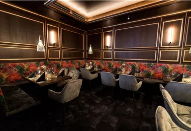 Ein stilvolles Restaurant mit eleganten Tischen und gemütlichen Sesseln. Die Wände sind mit einem farbenfrohen Muster dekoriert, und die Beleuchtung sorgt für eine warme Atmosphäre.