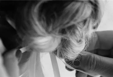 A person is putting a piece of clothing on another. The scene is in black and white and conveys an intimate atmosphere.