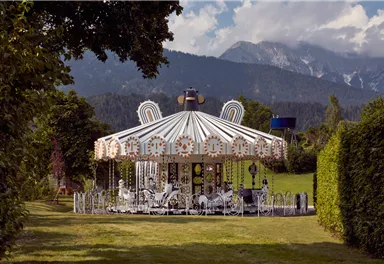 A nostalgic carousel in a green environment. In the background, mountains and a blue sky are visible.