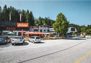 A bustling mountain station with a ticket area and numerous vehicles. The surroundings are green and surrounded by trees, ideal for outdoor activities.