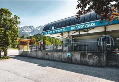 A cable car station in the mountain region with a view of the snowy mountains. The surroundings are green and inviting, ideal for excursions in nature.