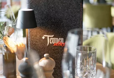 Ein eleganter Tisch in einem Restaurant mit einer Speisekarte und edlem Besteck. Im Hintergrund sind geschmackvoll dekorierte Stühle zu sehen.