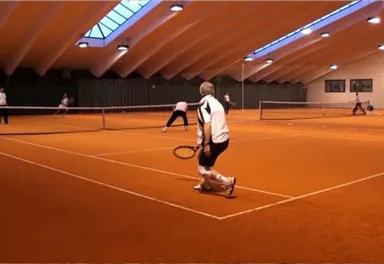 A tennis match in a hall with an orange floor covering. Several players are actively playing and focusing on the game.