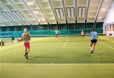 A tennis court in a hall with four players. The atmosphere is active and focused.