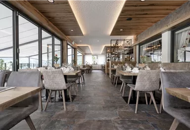 A modern restaurant with wooden decor and large windows. The tables are elegantly set and the space feels friendly and inviting.