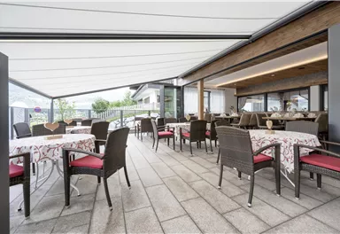An elegant restaurant with tables and chairs on a terrace. The surroundings are bright and inviting, ideal for relaxed outdoor meals.
