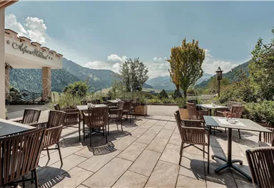 A cozy terrace with wooden furniture and a view of the mountains. The surroundings are green and inviting, perfect for a relaxed break.