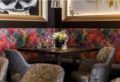 Ein eleganter Restauranttisch mit Blumen und Gläsern. Die Wände sind mit bunten, kunstvollen Mustern dekoriert.