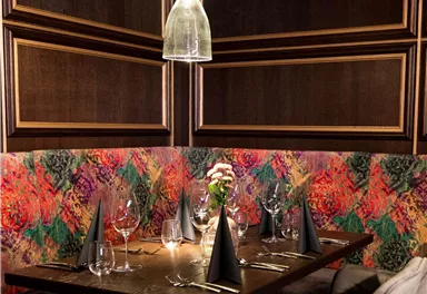 Ein elegantes Restaurant mit einem modernen Tisch und stilvollen Stühlen. Die Wände sind mit bunten Blumenmustern dekoriert, und die Tischdekoration ist ansprechend.