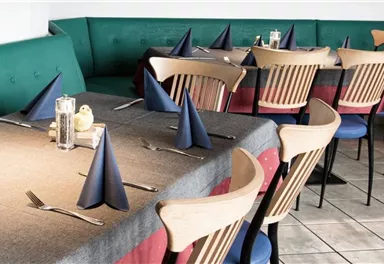 A cozy restaurant with tables decorated with gray tablecloths and blue napkins. The seating includes wooden chairs and a padded bench.