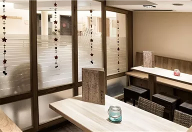 A cozy interior with wooden furniture and a modern design. A few decorative elements hang from the ceiling, and a table is adorned with a candle.