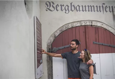 A couple stands in front of the entrance of the mining museum and looks curiously at a sign. The atmosphere is relaxed and inquisitive.