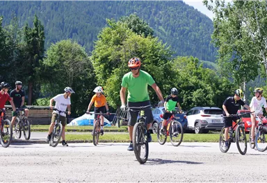 A group of cyclists is practicing in a green environment. In the foreground, a man in green clothing is riding a mountain bike.