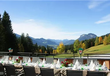 A beautiful view of green mountains and forests. A festively set table outdoors invites to a cozy meal.