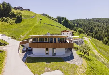 A modern house on a green hill, surrounded by trees and meadows. The architecture is stylish and offers a clear view of nature.